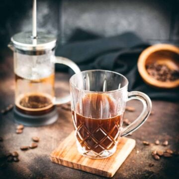 Delicious french press coffee in a glass mug, placed on a wooden coaster.