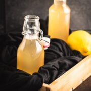 Beautiful preserving bottle, filled with vibrant lemon ginger syrup, placed in wooden crate.