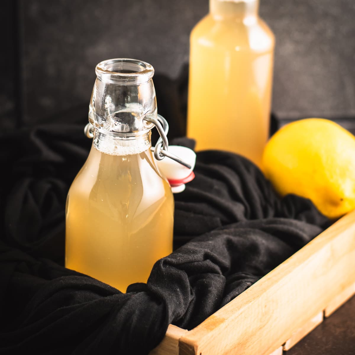 Beautiful preserving bottle, filled with vibrant lemon ginger syrup, placed in wooden crate.