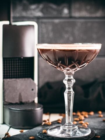 Cocktail glass, filled with a decadent Nespresso martini. Placed on a black slate plate, next to coffee beans.