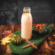 Pumpkin spice coffee creamer placed on green felt mat, next to pumpkins and cinnamon sticks.