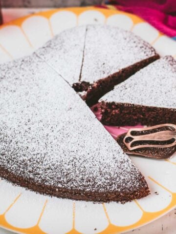 Delicious heart-shaped chocolate cake, dusted with powdered sugar. Ideal for Valentine's day! Placed on yellow-white serving plate.