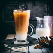 Gorgeous layered plant-based vanilla iced coffee, served in a beautiful glass, placed on a black slate plate.