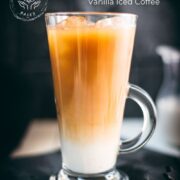 Gorgeous layered plant-based vanilla iced coffee, served in a beautiful glass, placed on a black slate plate.
