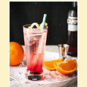Divine Campari Soda, placed on marbled serving plate. Garnished with a lemon twist and served with a drinking straw.