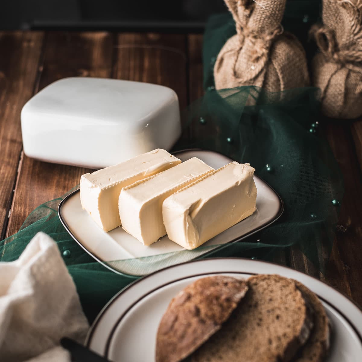 Butter, sliced on white plate with brown colored rim, next to a plate with sliced bread.