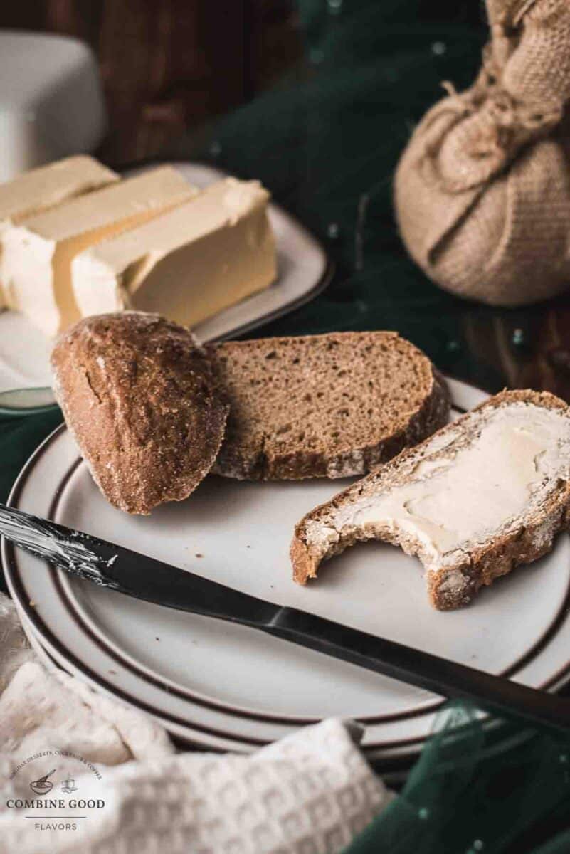 Buttered bread with a bite taken out of it, placed on a white plate with a brown rim.