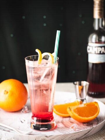Divine Campari Soda, placed on marbled serving plate. Garnished with a lemon twist and served with a drinking straw.