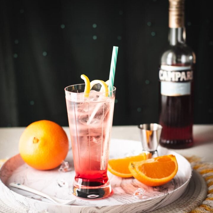 Divine Campari Soda, placed on marbled serving plate. Garnished with a lemon twist and served with a drinking straw.