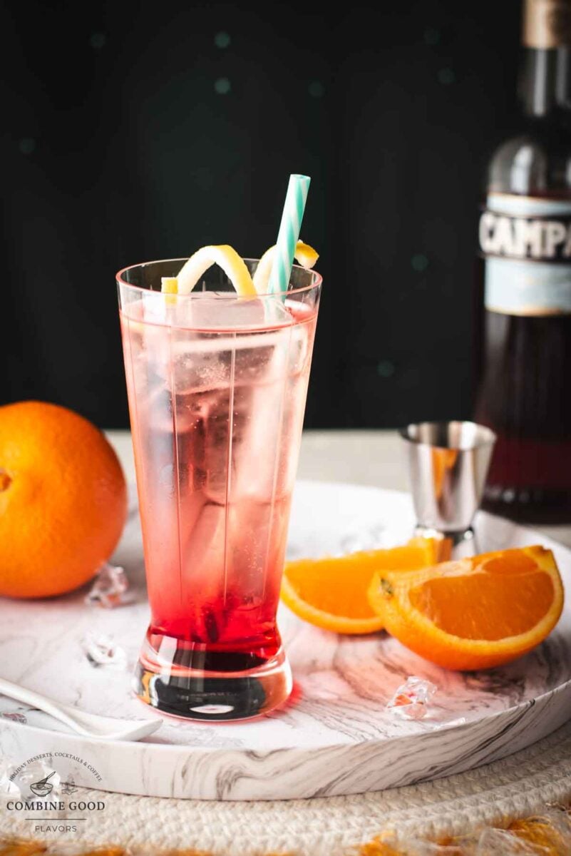 Divine Campari Soda, placed on marbled serving plate. Garnished with a lemon twist and served with a drinking straw.