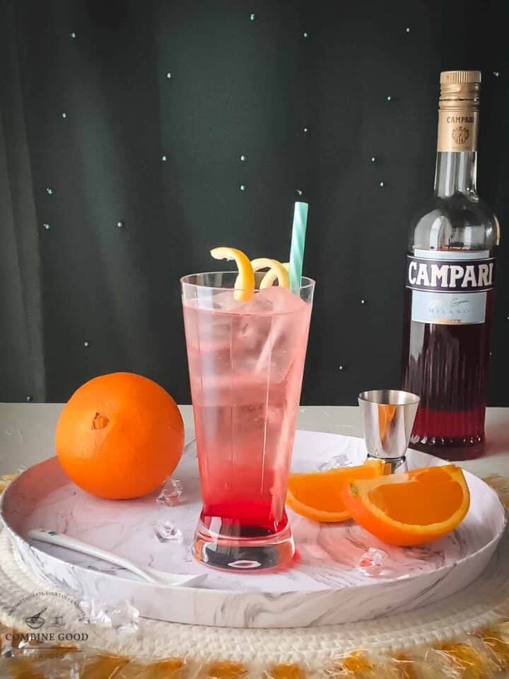 Divine Campari Soda, placed on marbled serving plate. Garnished with a lemon twist and served with a drinking straw.