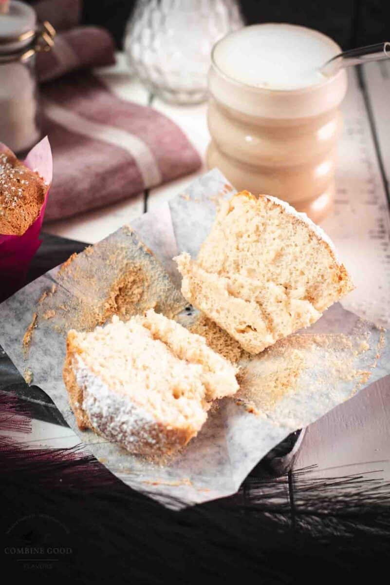 Light and fluffy angel food muffins with powdered sugar on a marbled plate, served with a cafe latte, one muffin cut in half to reveal the airy crumb.