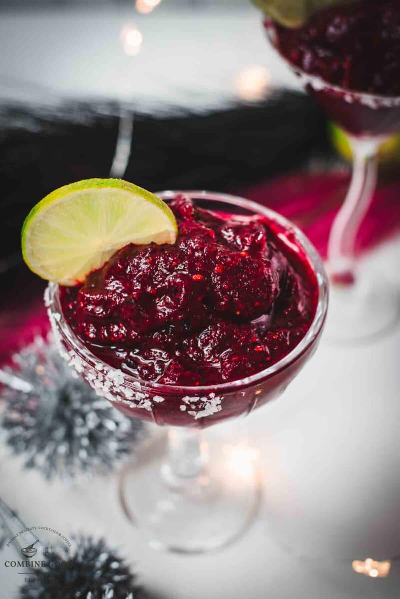 Magnificent frozen mixed berry margarita, served in cocktail glasses, garnished with a lime slice. With a vibrant dark red color. What an eye-catcher!
