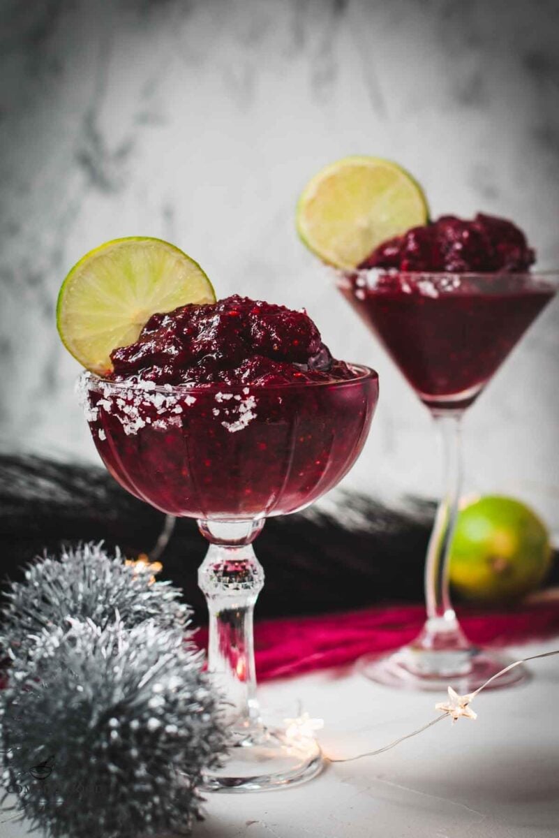 Magnificent frozen mixed berry margarita, served in cocktail glasses, garnished with a lime slice. With a vibrant dark red color. What an eye-catcher!