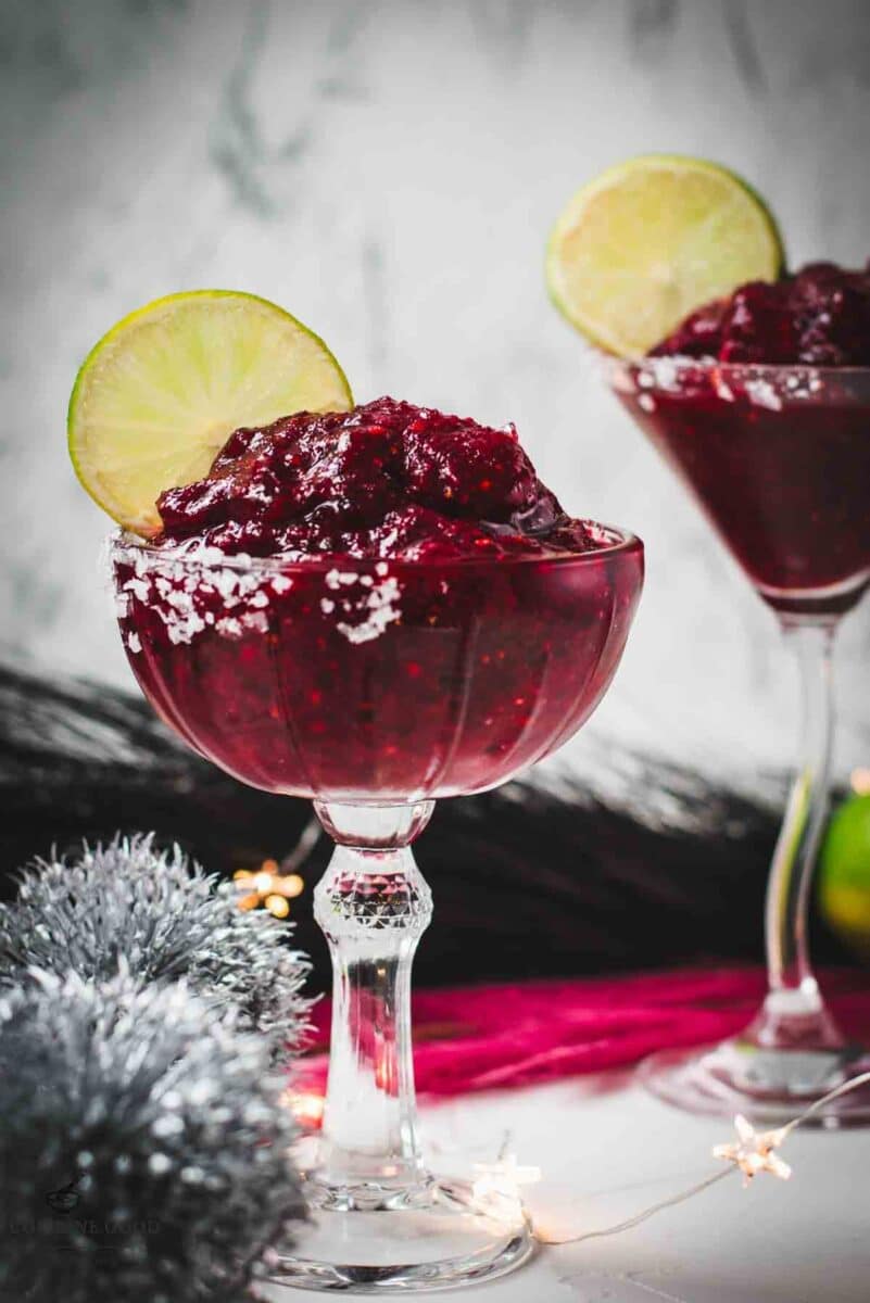 Magnificent frozen mixed berry margarita, served in cocktail glasses, garnished with a lime slice. With a vibrant dark red color. What an eye-catcher!