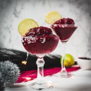 Magnificent frozen mixed berry margarita, served in cocktail glasses, garnished with a lime slice. With a vibrant dark red color. What an eye-catcher!