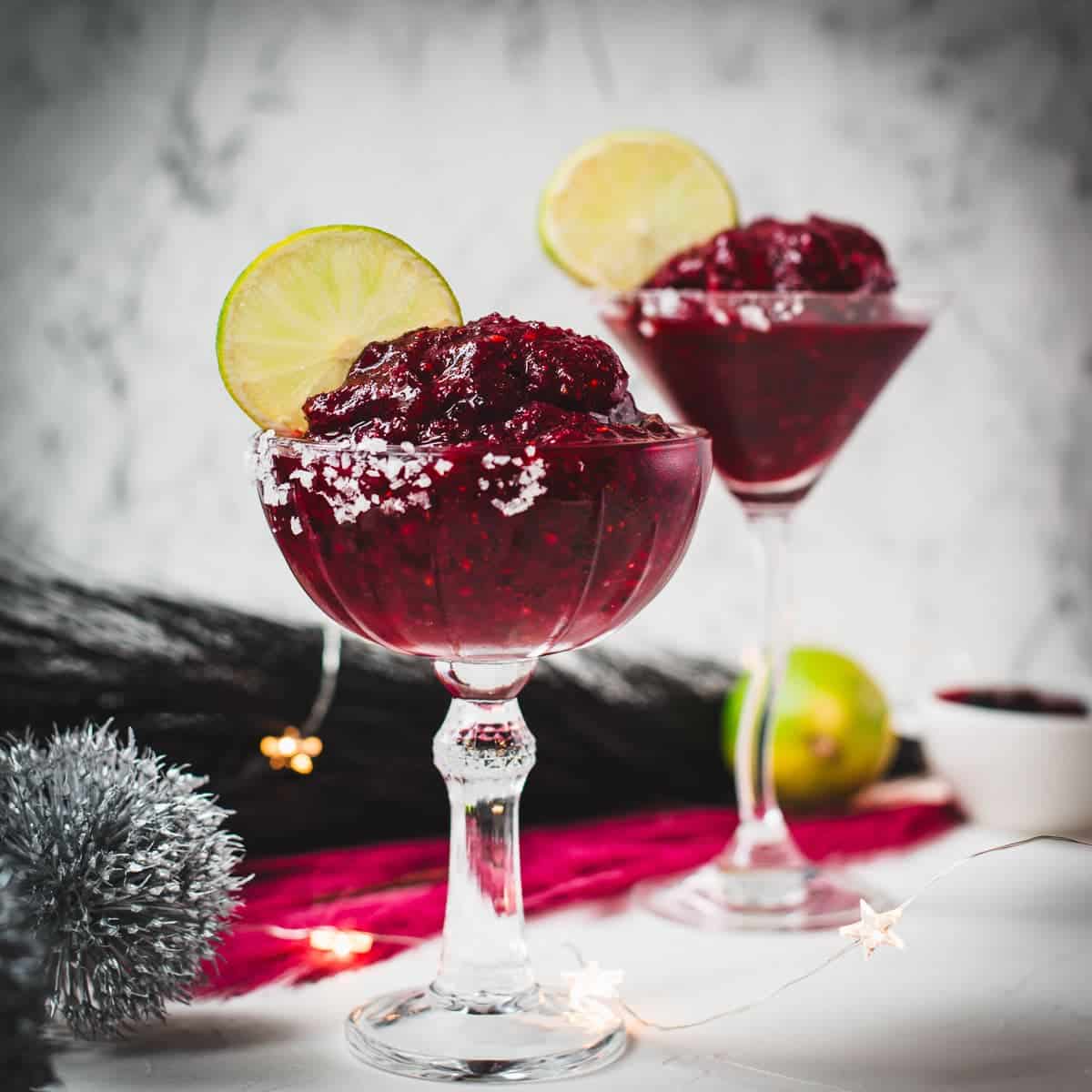Magnificent frozen mixed berry margarita, served in cocktail glasses, garnished with a lime slice. With a vibrant dark red color. What an eye-catcher!