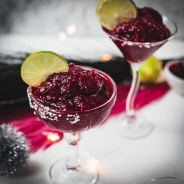 Magnificent frozen mixed berry margarita, served in cocktail glasses, garnished with a lime slice. With a vibrant dark red color. What an eye-catcher!