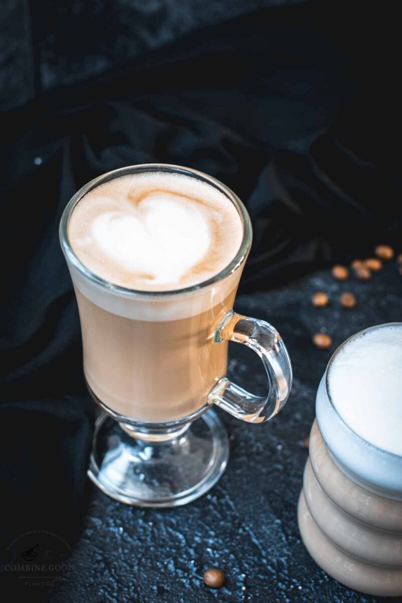 2 glasses filled with delicious vanilla latte. placed on dark ground. Left on has a latte art heart on top.