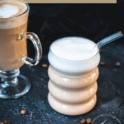 2 glasses filled with delicious vanilla latte. placed on dark ground. Left on has a latte art heart on top.