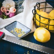 Zested lemon next to a lemon zester and a bowl full of lemons.