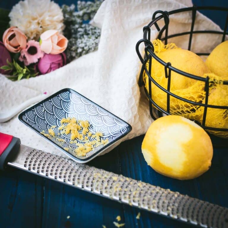 Zested lemon next to a lemon zester and a bowl full of lemons.