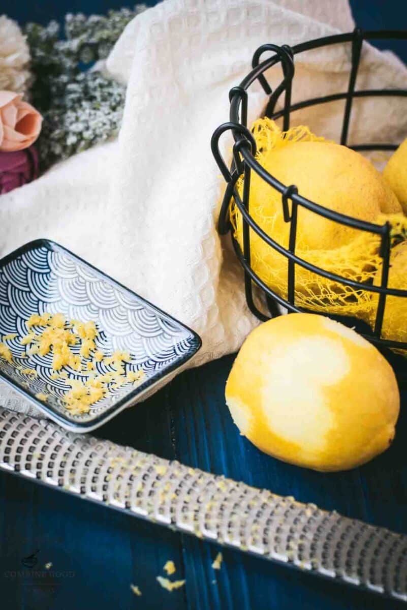 Zested lemon next to a lemon zester and a bowl full of lemons.