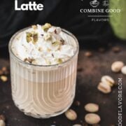 Divine pistachio latte with pistachio liqueur, served in beautiful drinking glass, resting on dark surface scattered with coffee beans and pistachios.