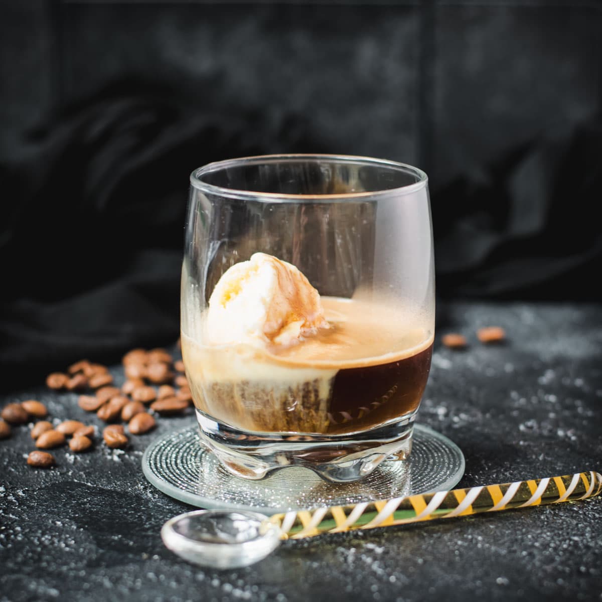 A scoop of vanilla ice cream sits in a glass of dark espresso on a black surface, making a perfect affogato.