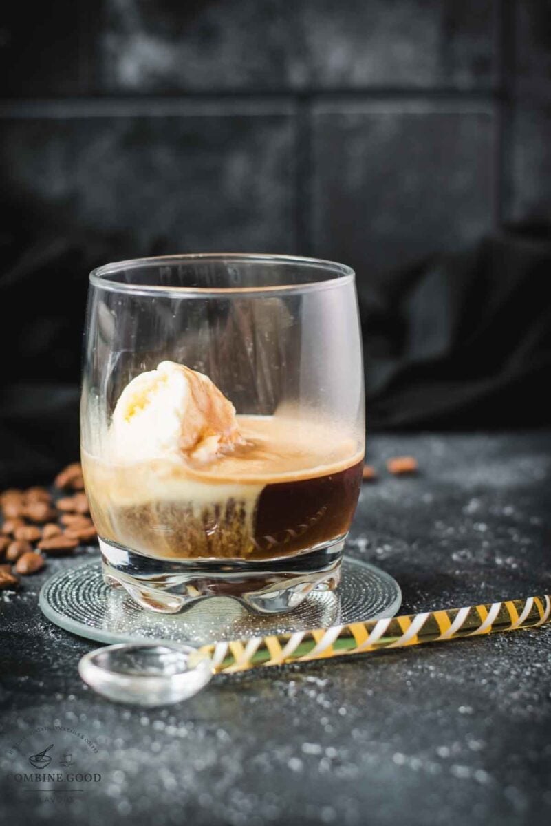 A scoop of vanilla ice cream sits in a glass of dark espresso on a black surface, making a perfect affogato.