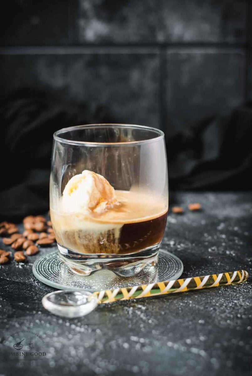 A scoop of vanilla ice cream sits in a glass of dark espresso on a black surface, making a perfect affogato.