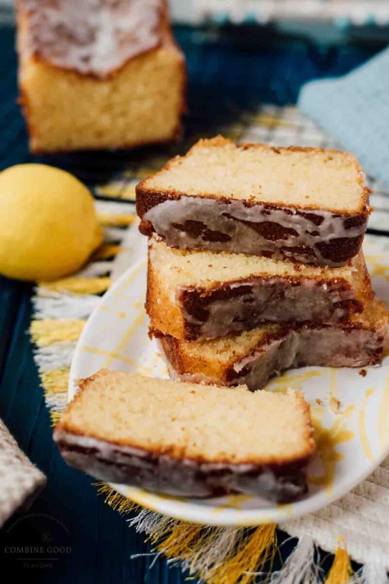 Sliced and stacked lemon loaf cake slices, placed on white and yellow plate, next to a lemon.