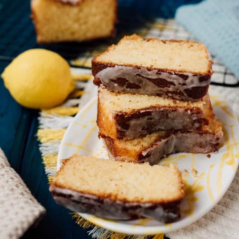 Sliced and stacked lemon loaf cake slices, placed on white and yellow plate, next to a lemon.