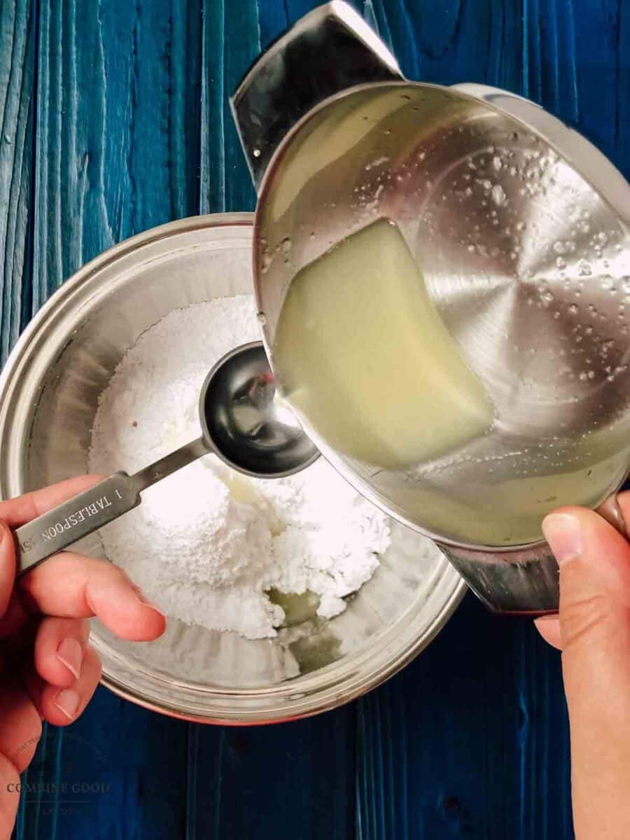 Measuring one tablespoon of freshly squeezed lemon juice above a bowl of powdered sugar.