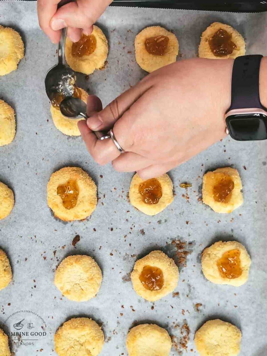 Filling the coconut cream cheese cookies with fig jam using two teaspoons.