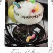 Close-up of gummy worms peeking from the vivid green frozen cocktail beside the coarse black sugar rim.