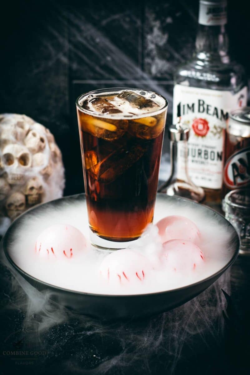 Bourbon and root beer Halloween cocktail with bourbon and root beer bottles in the background.