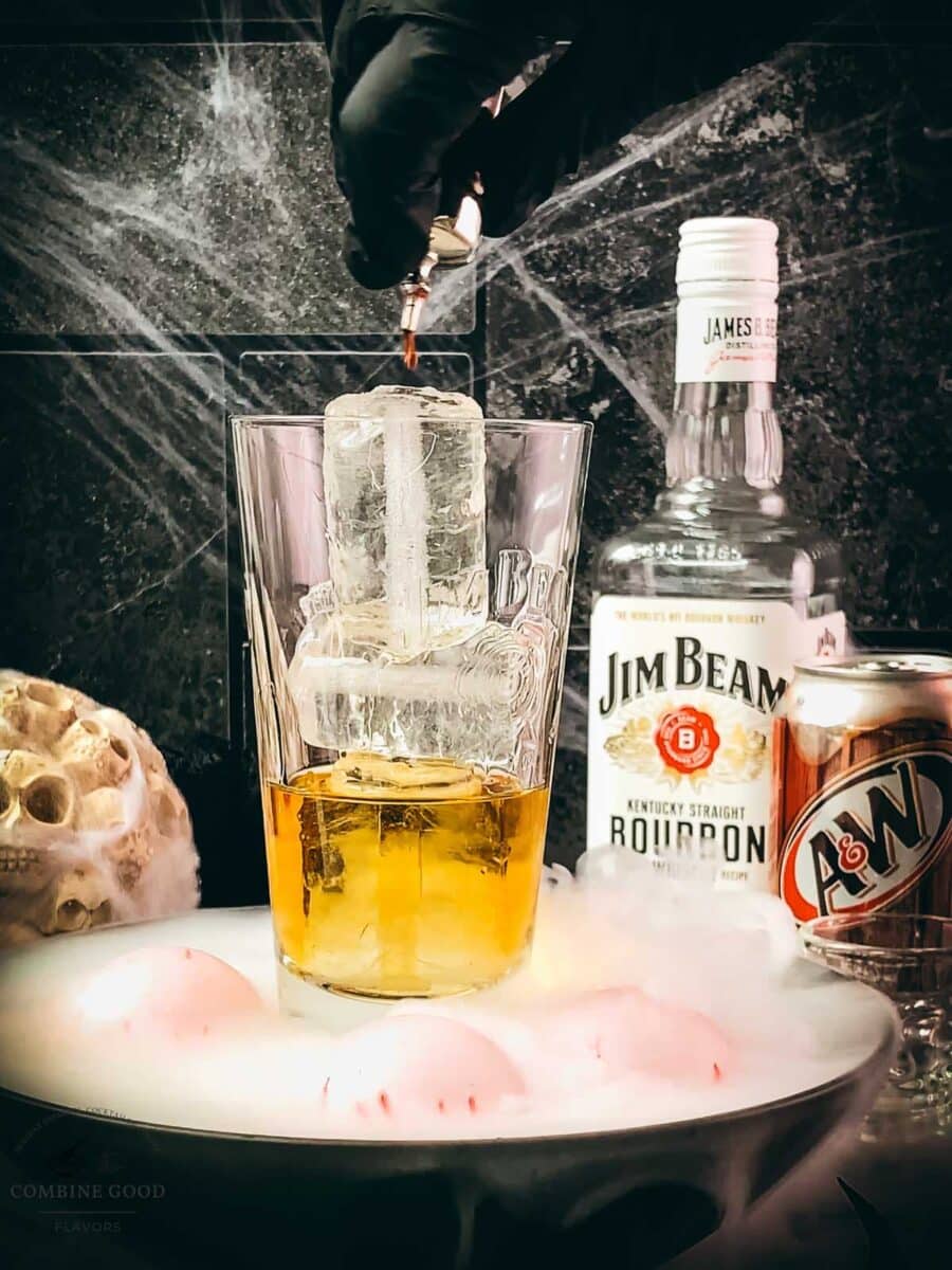 Angostura bitters being added to bourbon and ice in a cocktail glass.