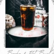 Halloween bourbon and root beer cocktail surrounded by smoke, dragon eyes, skulls, and spiderwebs.