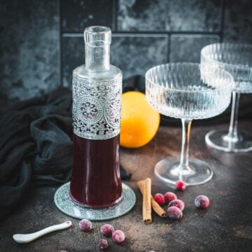 Finished cranberry simple syrup with frozen cranberries and cinnamon on a dark background.