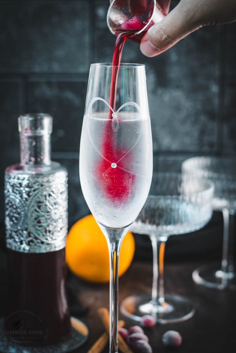 Cranberry simple syrup being poured into a tall glass of sparkling water