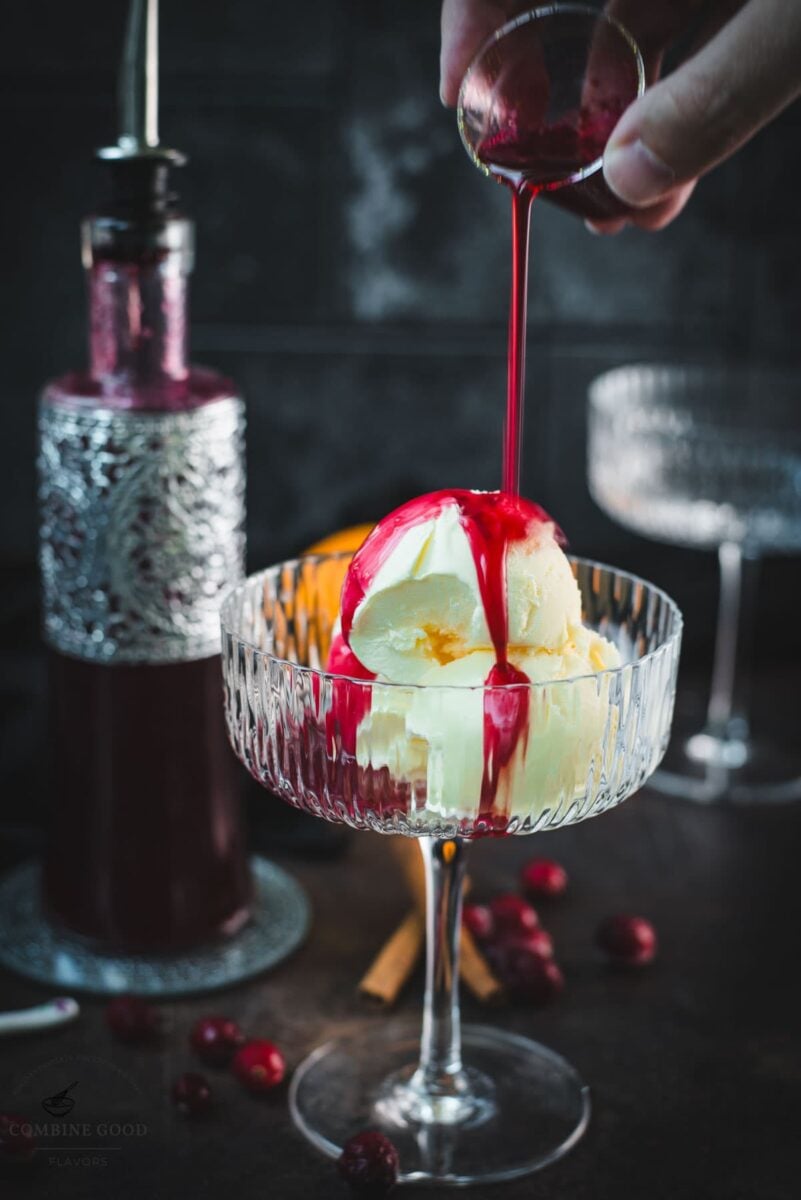 Cranberry simple syrup being poured over vanilla ice cream in a cocktail glass