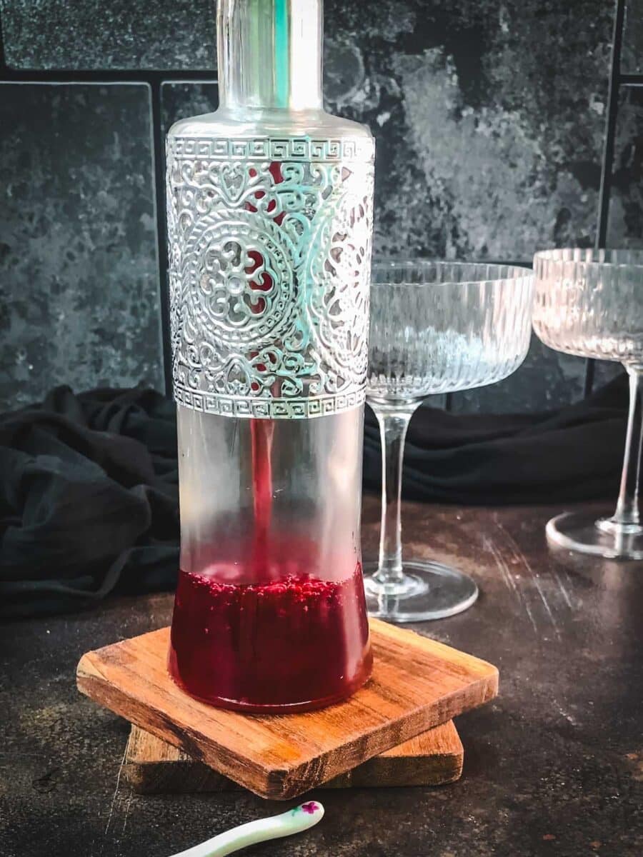 Pouring finished cranberry simple syrup into a glass preserving bottle