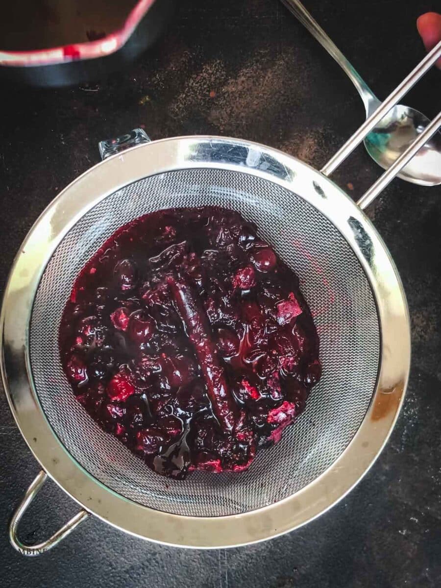 Cooked cranberries and mixed berries draining in a fine-mesh sieve