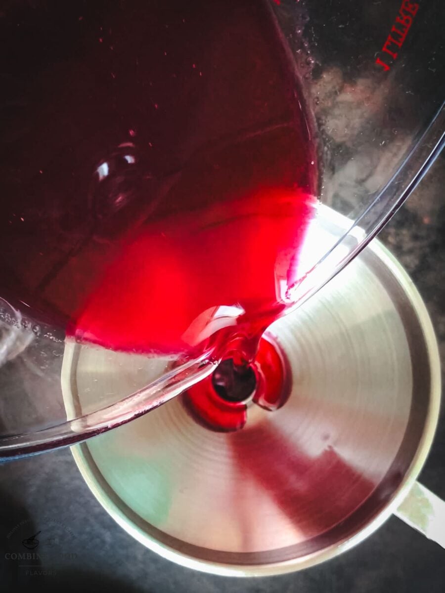 Pouring strained cranberry simple syrup through a funnel into a glass bottle