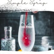Cranberry simple syrup being poured into a tall glass of sparkling water