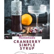 Homemade cranberry simple syrup in a decorative glass bottle with frozen cranberries, cinnamon, and orange