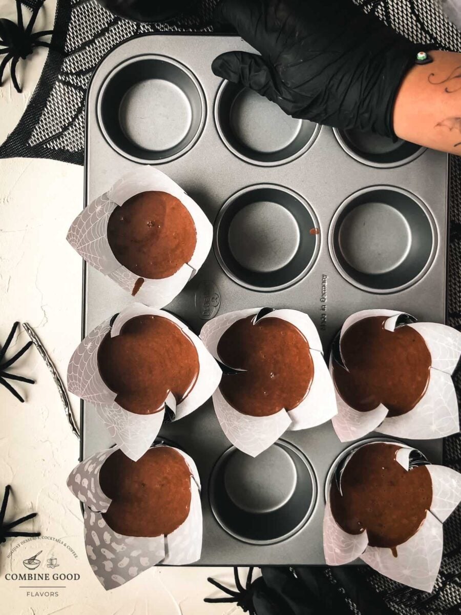 Gloved hands holding a muffin tray filled with chocolate root beer batter