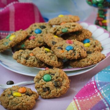 Soft oatmeal M&M cookies with chocolate chips stacked on a plate with colorful spring tulips and M&M’s in the background.