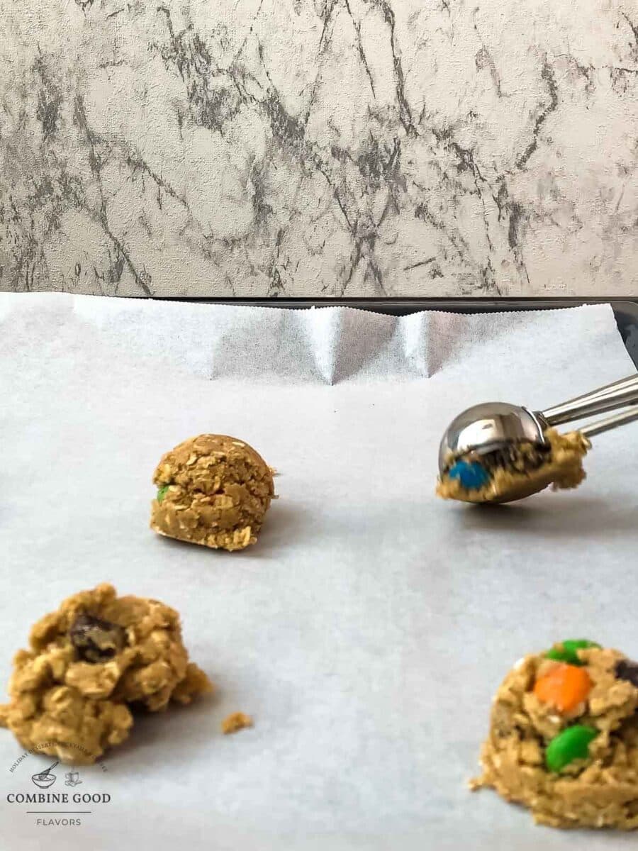 Scooping chilled oatmeal M&M cookie dough on a parchment-lined baking sheet.